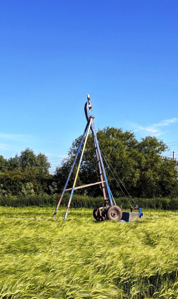 CJ Associates cable percussion drilling rig, set out in a field on site, with the blue sky in the background.