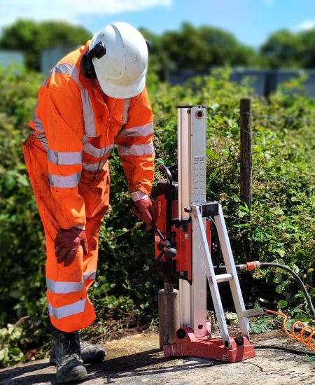 Concrete Coring CJ Associates worker dressed in hi-vis clothing and personal protective equipment, completing concrete coring, with greenery in the background.